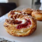A close-up of a flaky Gluten-Free Strawberry Cream Cheese Danish topped with jam and powdered sugar.
