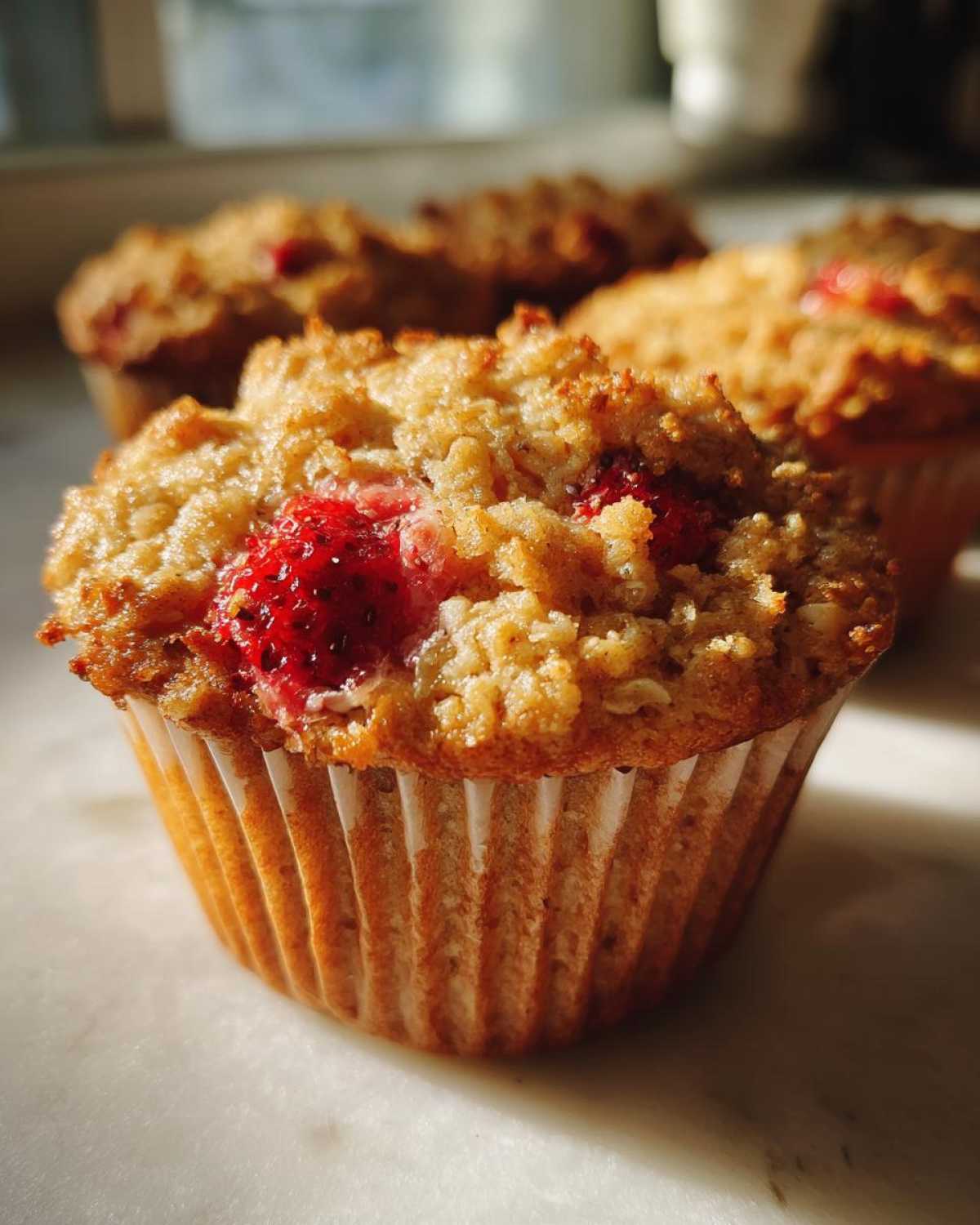A close-up of a freshly baked Gluten-Free Strawberry Oat Muffin with a crumbly top and visible strawberry pieces.