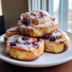 A close-up stack of four freshly baked Blueberry Cinnamon Rolls covered in thick white icing.