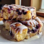 A stack of three gooey Blueberry Cinnamon Rolls generously topped with white icing, sitting on a white plate.