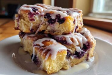 A stack of three gooey Blueberry Cinnamon Rolls generously topped with white icing, sitting on a white plate.