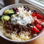 A vibrant Greek Ground Beef Rice Bowl featuring seasoned meat, rice, cucumber, tomatoes, olives, feta, and a dollop of tzatziki.