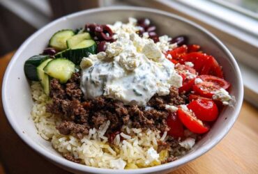 A vibrant Greek Ground Beef Rice Bowl featuring seasoned meat, rice, cucumber, tomatoes, olives, feta, and a dollop of tzatziki.