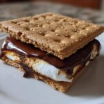 A close-up of a gooey HERSHEY'S S'mores sandwich featuring a toasted marshmallow, melted chocolate, and graham crackers.