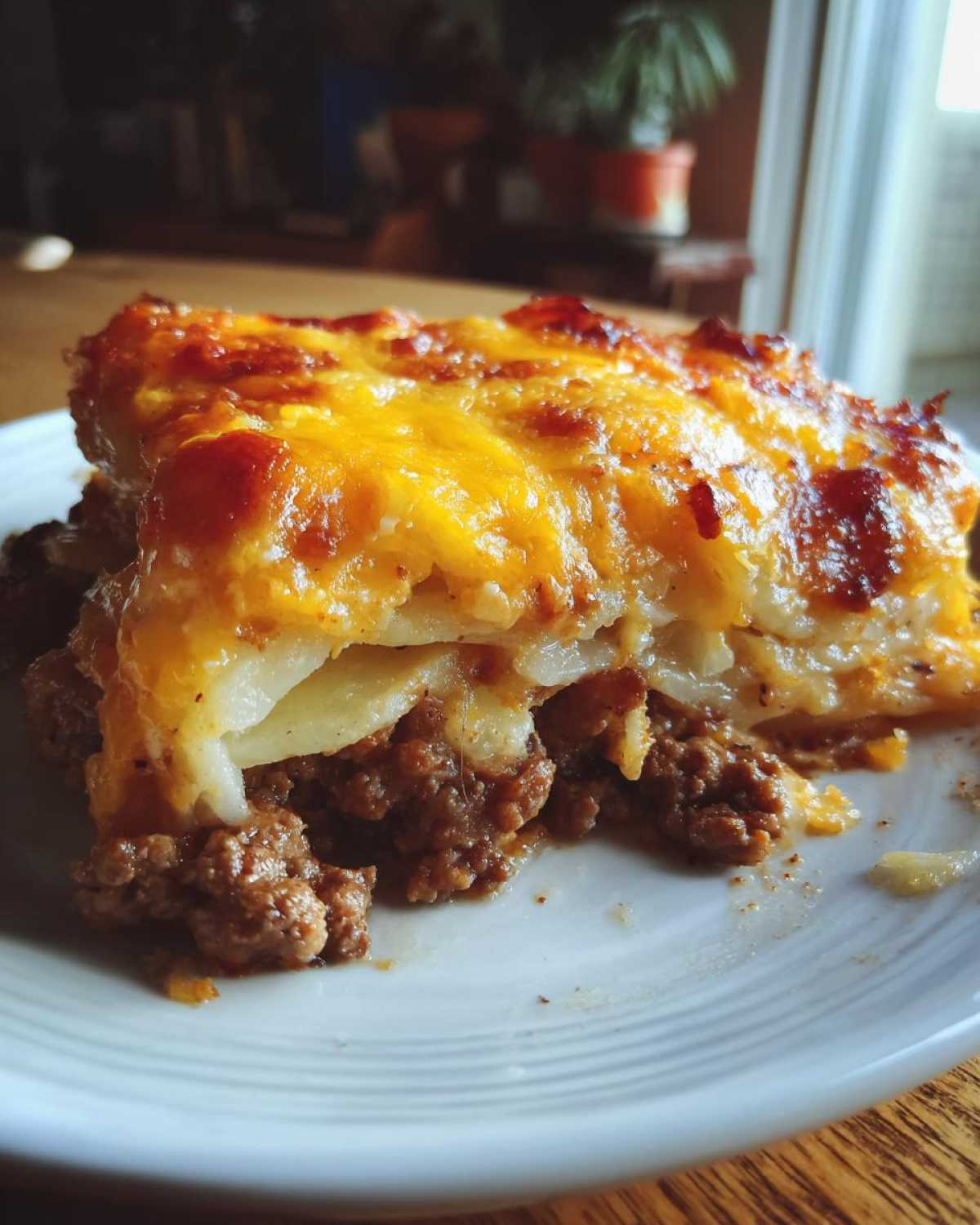 A close-up slice of Hobo Casserole Beef Potato Dish Comfort topped with melted, browned cheddar cheese.