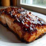 A close-up of a perfectly cooked Honey Soy Glazed Salmon fillet with a thick, shiny, caramelized glaze on a white plate.