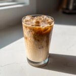 A tall glass filled with an Iced Honey Vanilla Latte with Oat Milk, showing swirling layers of espresso and creamy milk over ice.