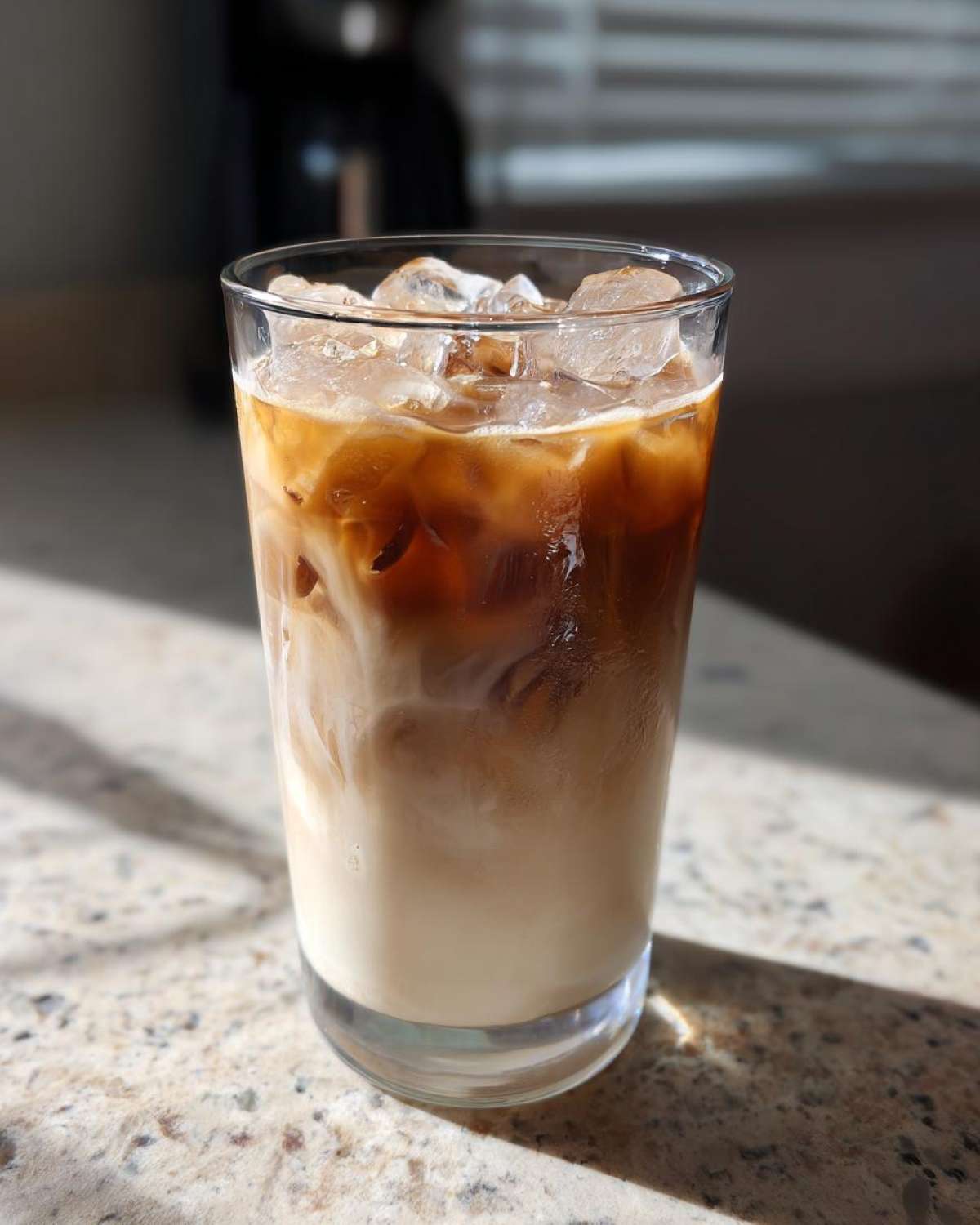 Close-up of a tall glass filled with an Iced Honey Vanilla Latte with Oat Milk, showing layers of espresso and milk swirling over ice.
