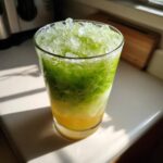 A tall glass filled with a layered Iced Matcha Pineapple Refresher, topped with crushed ice.