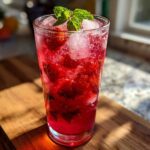 A tall glass filled with vibrant red Iced Strawberry Hibiscus Tea Lemonade, ice, and fresh mint garnish.