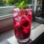 Tall glass of vibrant Iced Strawberry Hibiscus Tea Lemonade filled with ice, strawberries, and topped with fresh mint.