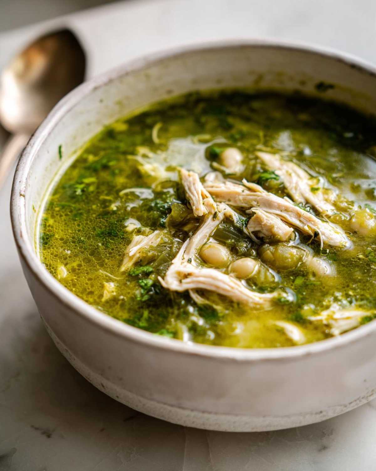 A close-up of a rustic bowl filled with vibrant green Instant Pot Chicken Pozole Verde, showing shredded chicken and hominy.