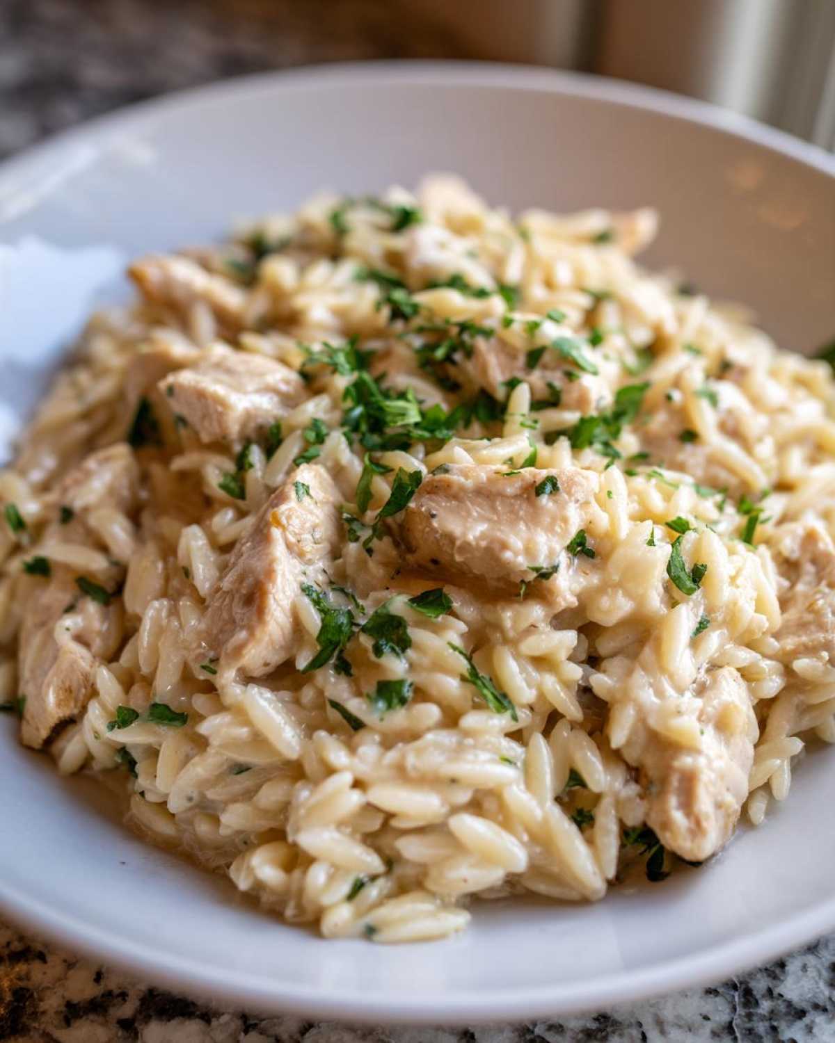 A close-up of Instant Pot Creamy Chicken and Orzo, featuring tender chicken pieces mixed with creamy orzo pasta and topped with fresh parsley.