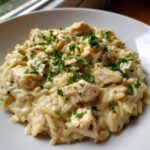 A close-up of creamy Instant Pot Creamy Chicken and Orzo topped with fresh parsley in a white bowl.