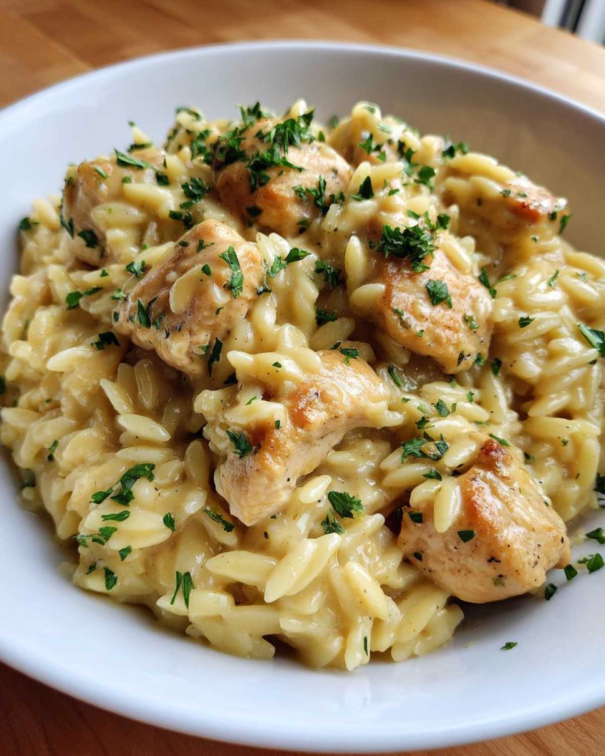 A close-up of a white bowl filled with creamy Instant Pot Creamy Chicken and Orzo, garnished with fresh parsley.