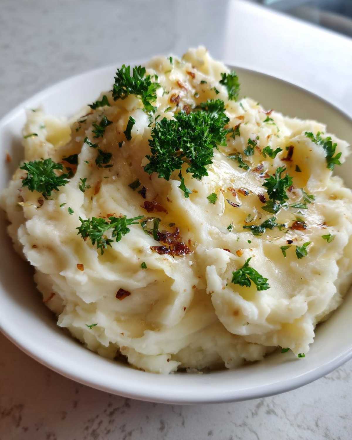 A close-up of creamy Instant Pot Creamy Garlic Butter Potatoes topped with melted butter, herbs, and browned garlic bits.