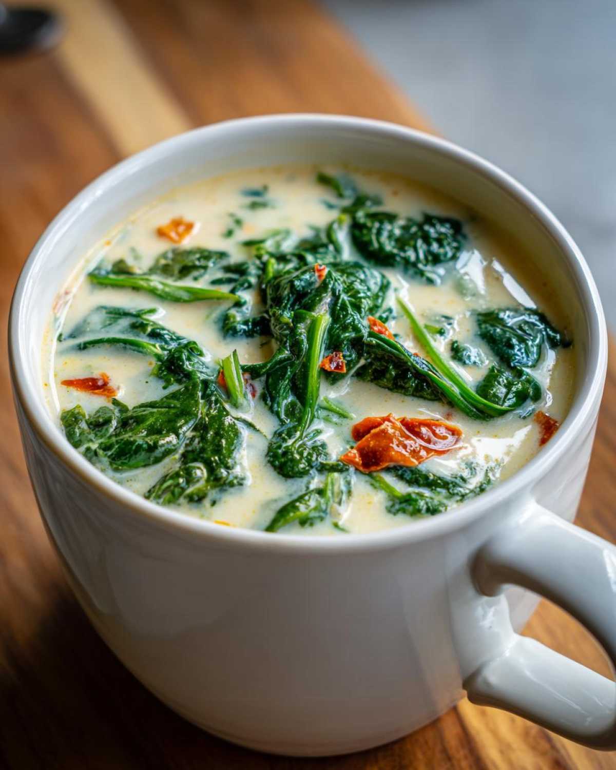 Close-up of a white mug filled with Instant Pot Creamy Tuscan White Bean Soup, featuring spinach and sun-dried tomatoes.
