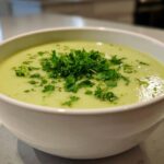 A close-up of a bowl of smooth, pale green Julia Child Potato Leek Soup topped with fresh chopped parsley.