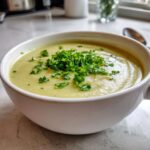 A close-up of creamy Julia Child Potato Leek Soup topped generously with fresh chopped parsley in a white bowl.