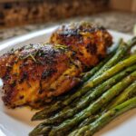 Two crispy, seasoned chicken thighs served next to bright green asparagus, perfect for a Keto Air Fryer Quick Low Carb Dinner.