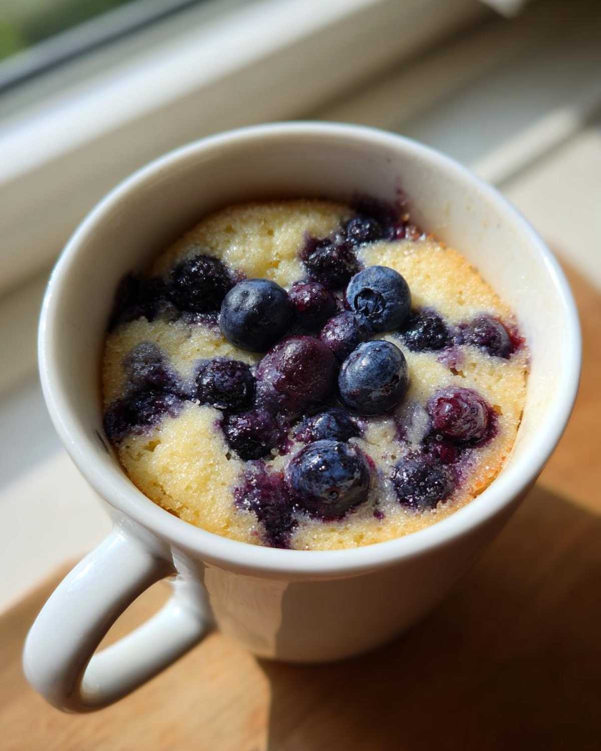 Close-up of a freshly baked Keto Blueberry Lemon Mug Cake topped with whole blueberries.