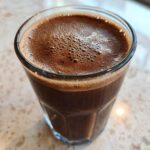 Close-up of a rich, dark brown Keto Creamy Chocolate Peanut Butter Shake with a frothy top in a clear glass.