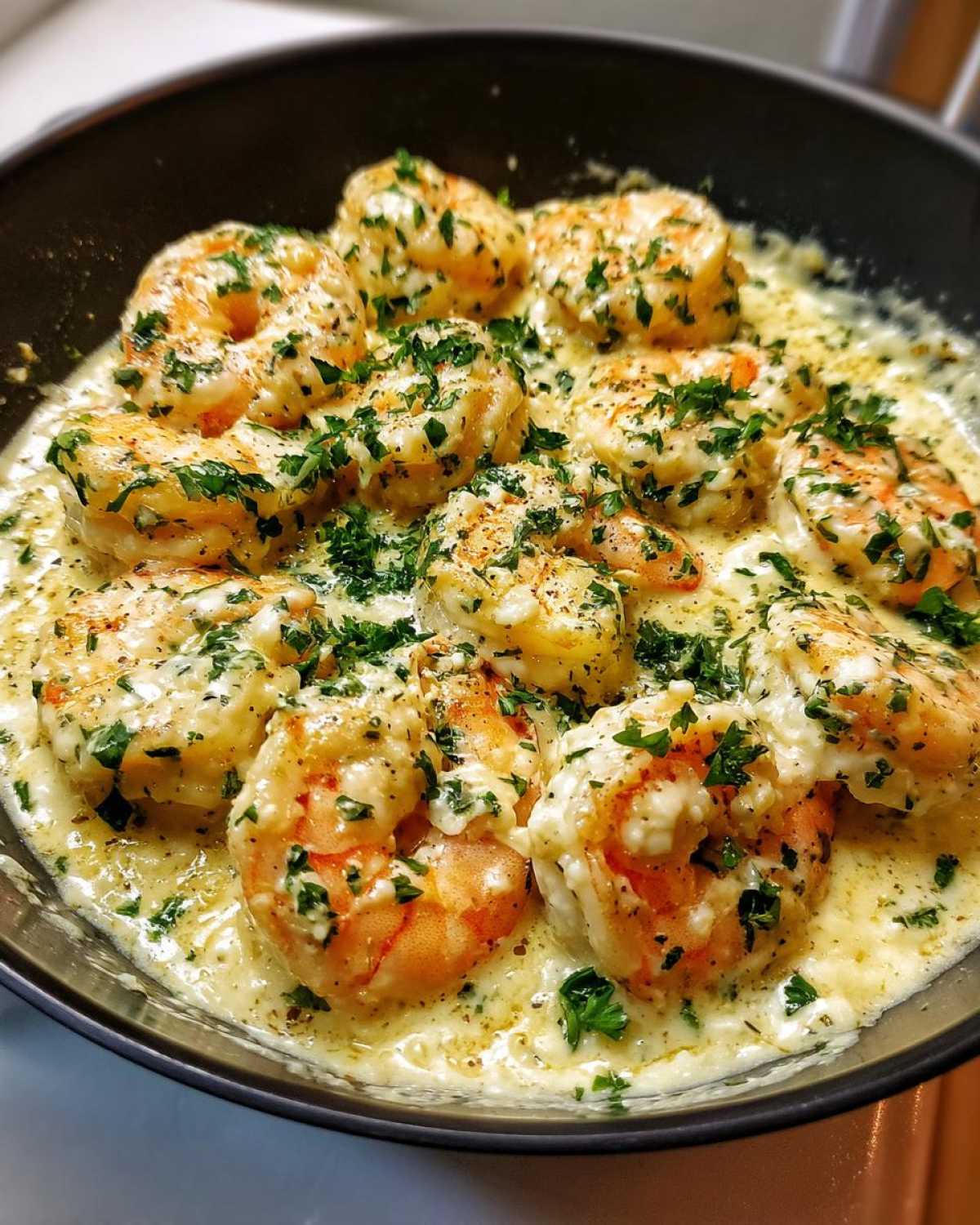 Close-up of plump shrimp coated in a rich, creamy garlic sauce and topped with fresh parsley, ready to serve from the skillet.