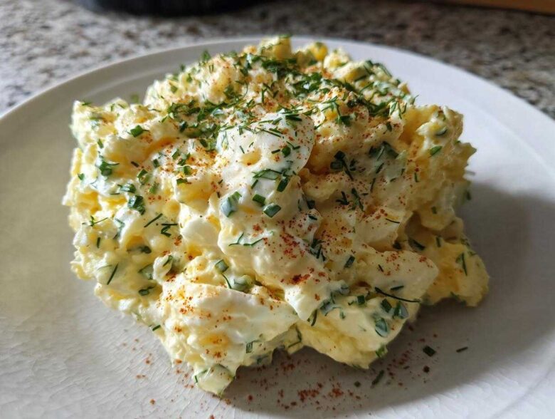 A scoop of rich Keto Creamy Herb Deviled Egg Salad topped with fresh chives and paprika on a white plate.