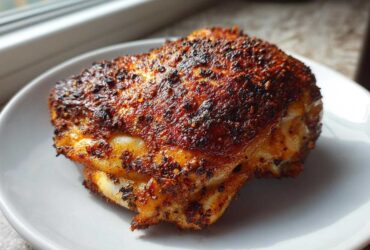 A close-up of a single, perfectly cooked Keto Crispy Baked Chicken Thighs with a dark, seasoned, crispy skin.