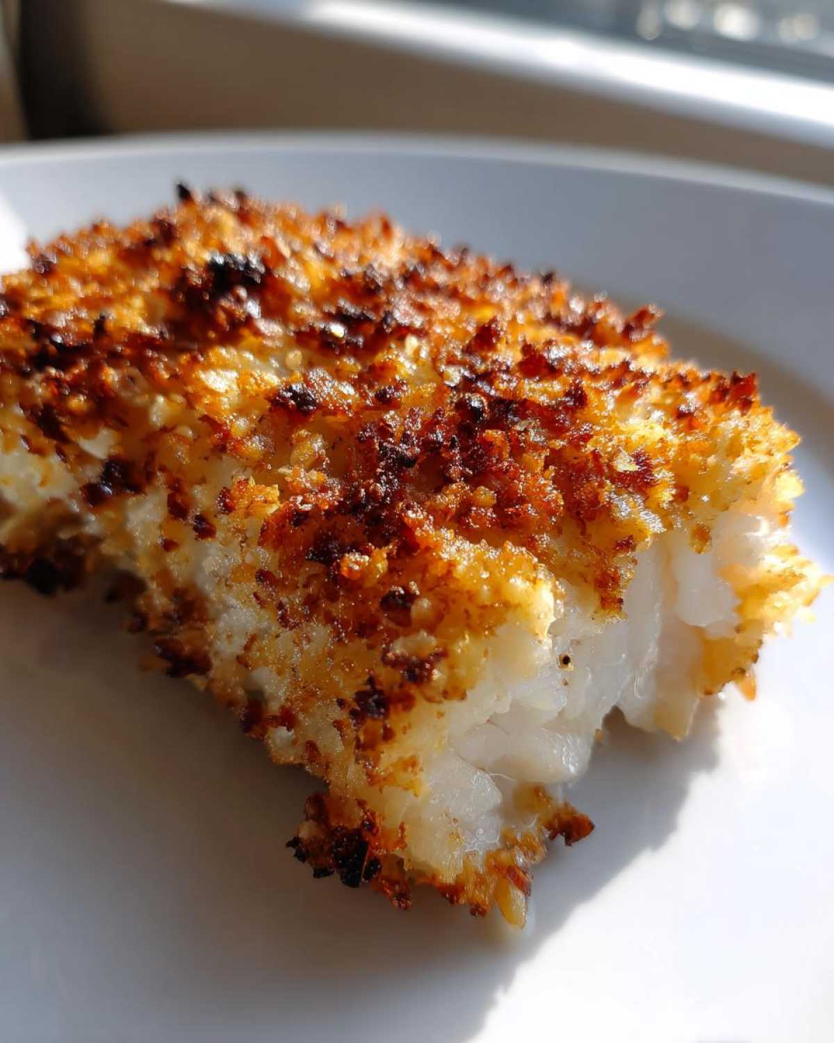 Close-up of a flaky white fish fillet with a golden brown, crispy Keto Crispy Parmesan Crusted Cod topping.