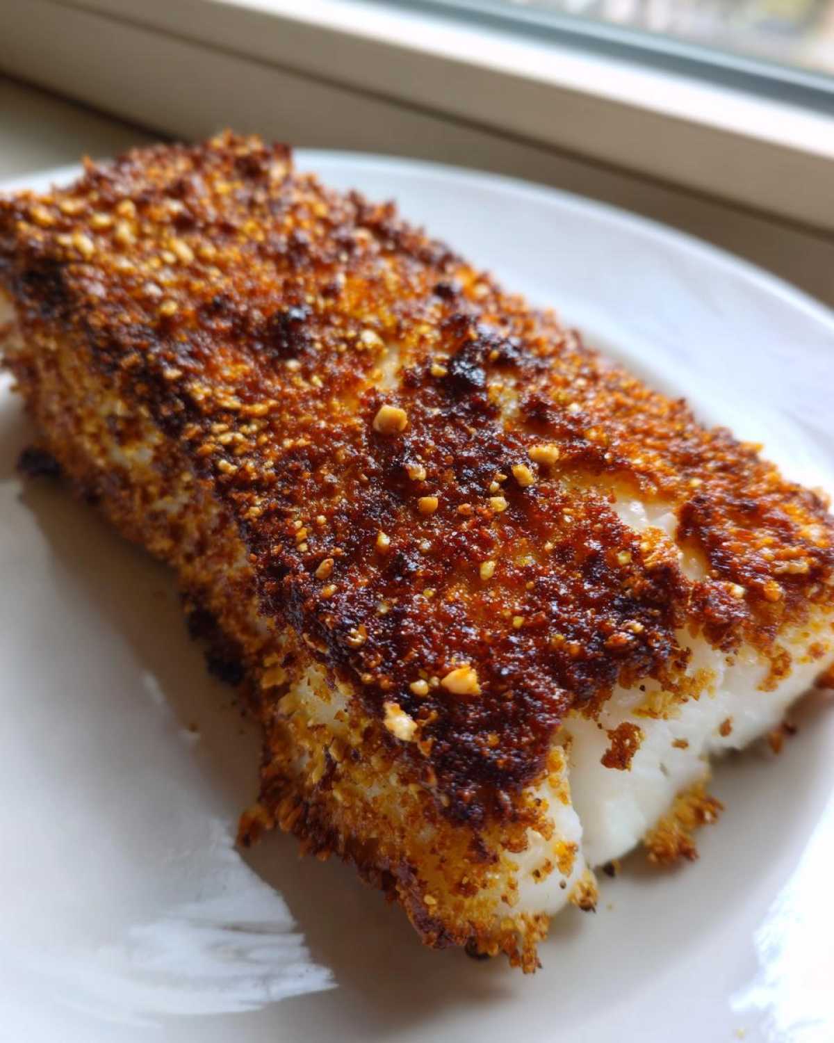 Close-up of a perfectly cooked Keto Crispy Parmesan Crusted Cod fillet with a dark golden, crunchy topping.
