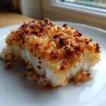 A close-up of a perfectly baked fillet of Keto Crispy Parmesan Crusted Cod on a white plate.