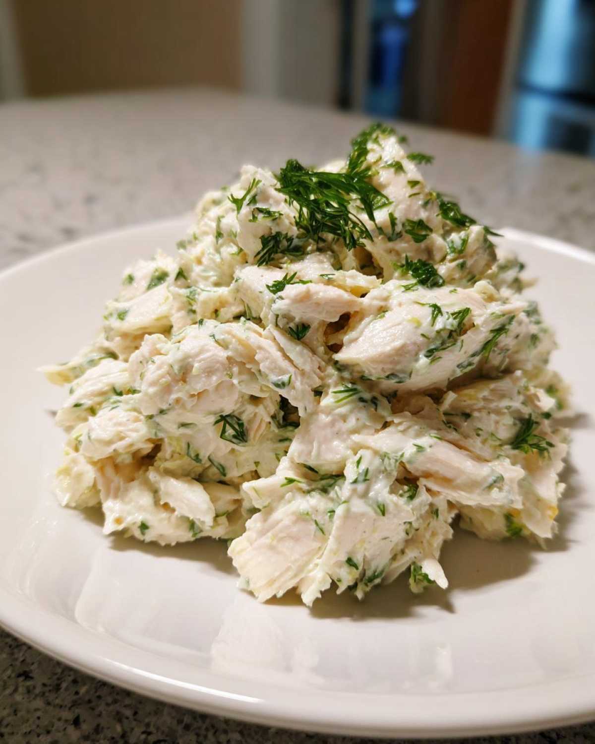 A mound of creamy Keto Lemon Herb Chicken Salad, featuring shredded chicken mixed with herbs and topped with fresh dill.