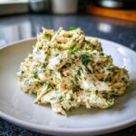 A mound of creamy Keto Lemon Herb Chicken Salad mixed with fresh green herbs on a white plate.