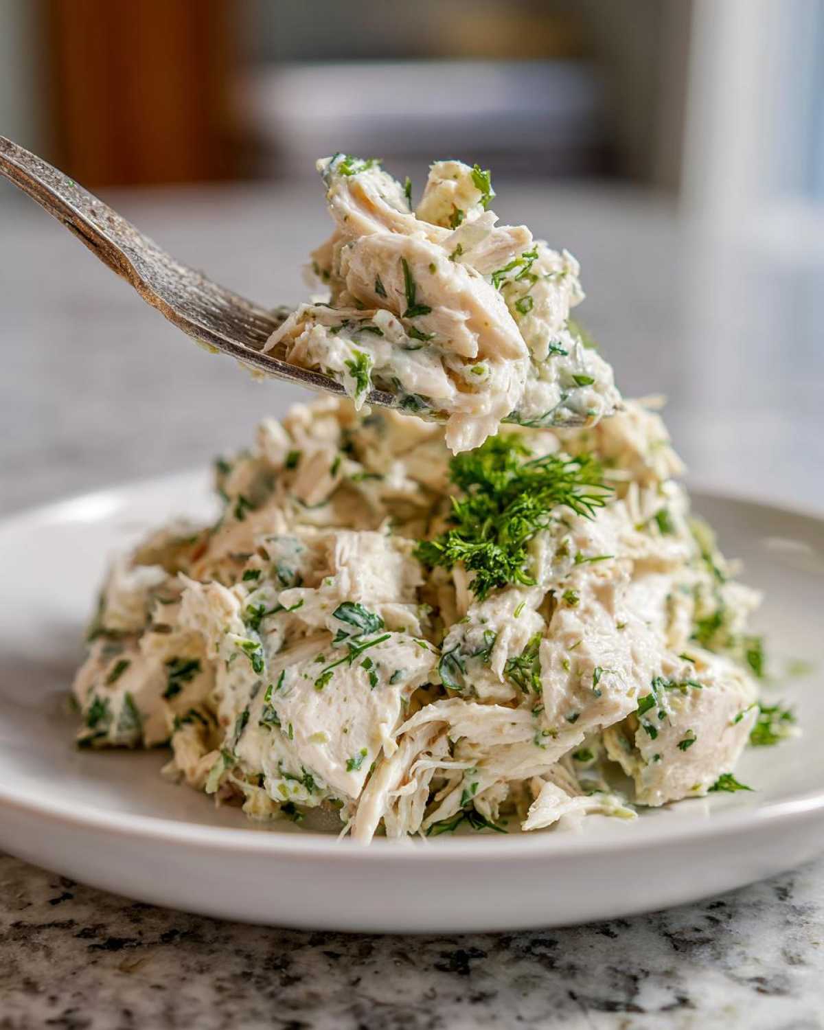 A fork lifting a bite of creamy Keto Lemon Herb Chicken Salad mixed with fresh green herbs.