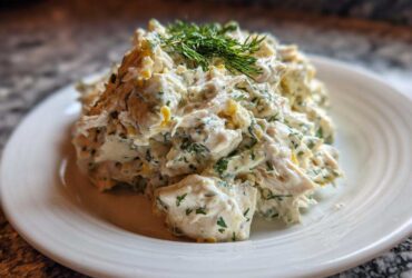 A mound of creamy Keto Lemon Herb Chicken Salad garnished with fresh dill on a white plate.