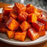 Close-up of shiny, caramelized cubes of Maple Roasted Sweet Potatoes piled on a white plate.