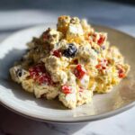 Close-up of a scoop of creamy Memorial Day Egg Salad mixed with chopped red peppers and dark olives on a light plate.