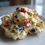 A scoop of creamy Memorial Day Egg Salad featuring chunks of egg, red bell pepper, and blueberries on a white plate.