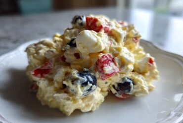 A scoop of creamy Memorial Day Egg Salad featuring chunks of egg, red bell pepper, and blueberries on a white plate.