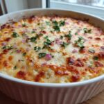 Close-up of a baked Mexican Street Corn Dip in a white oval dish, topped with melted, browned cheese, diced red onion, and cilantro.