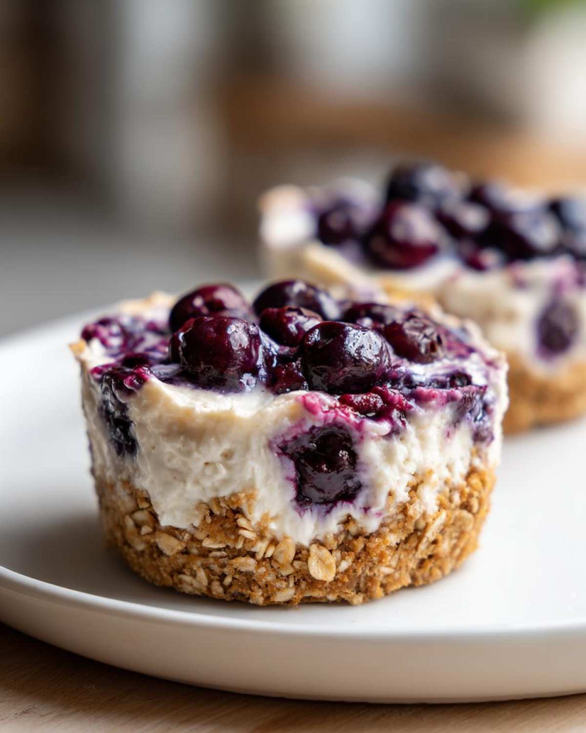 A close-up of a single No-Bake Blueberry Cheesecake Oat Cup featuring a thick oat crust and creamy filling topped with glossy blueberries.