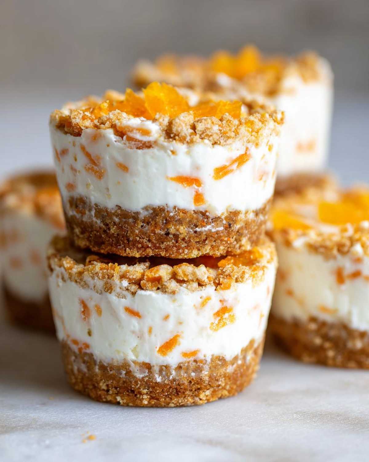 Two No-Bake Carrot Cake Cheesecake Cups are stacked, showing the graham cracker crust, creamy filling with shredded carrots, and crumb topping.