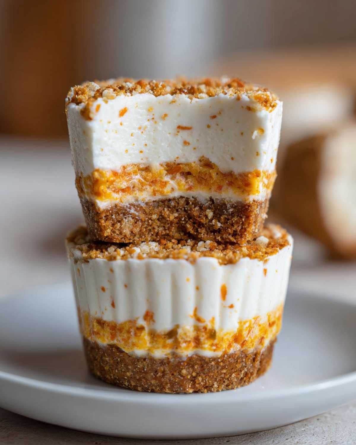 Two stacked No-Bake Carrot Cake Cheesecake Cups shown in cross-section revealing graham crust, carrot layer, and cream cheese topping.