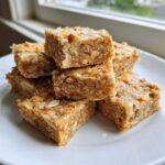 A stack of six chewy No-Bake Lemon Almond Date Bars studded with almonds and orange zest on a white plate.