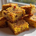 Close-up of stacked, golden-brown No-Bake Lemon Almond Date Bars with visible dried fruit pieces on a white plate.
