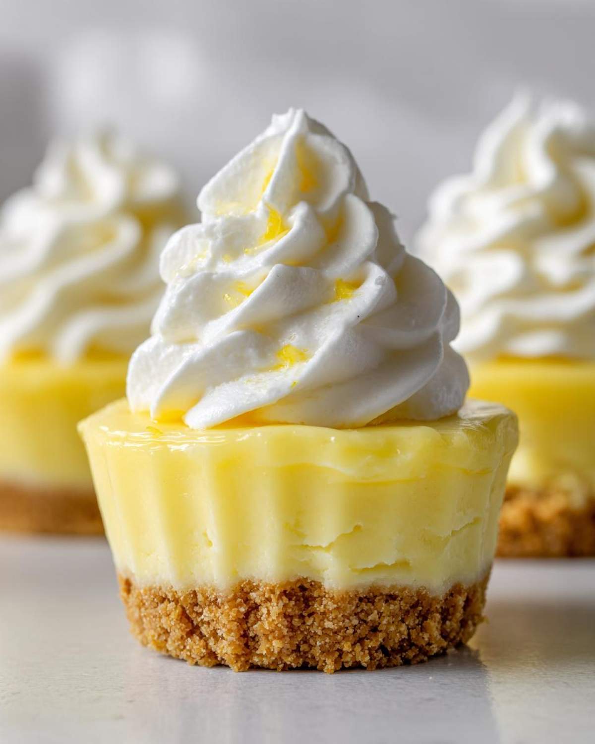 A single, vibrant No-Bake Lemon Cream Pie Cup featuring a graham cracker crust, bright yellow filling, and a swirl of whipped cream.