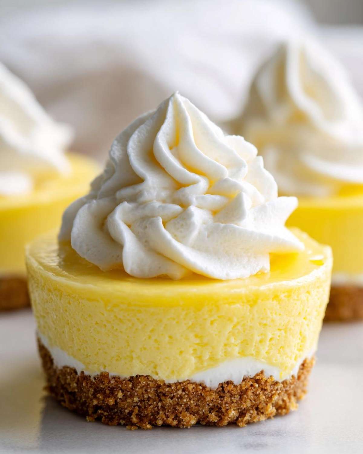 A close-up of a single No-Bake Lemon Cream Pie Cup topped with a swirl of whipped cream.