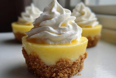 A close-up of one of the No-Bake Lemon Cream Pie Cups featuring a bright yellow filling, graham cracker crust, and a swirl of whipped cream.