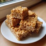 A stack of chewy No-Bake Peanut Butter Rice Cereal Bars on a white plate.